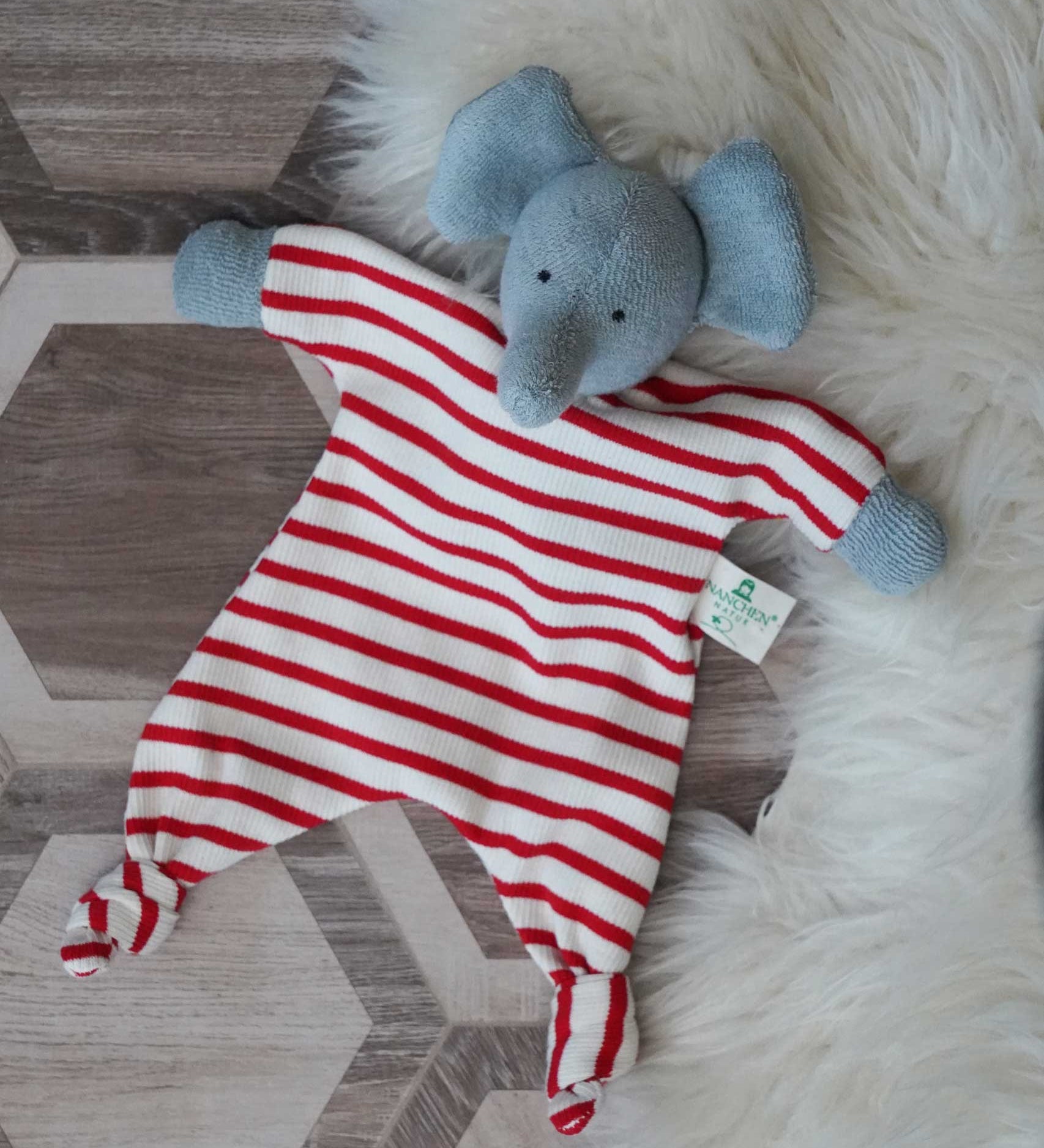 A Nanchen elephant baby comforter soft toy placed on a rug on a wooden floor.