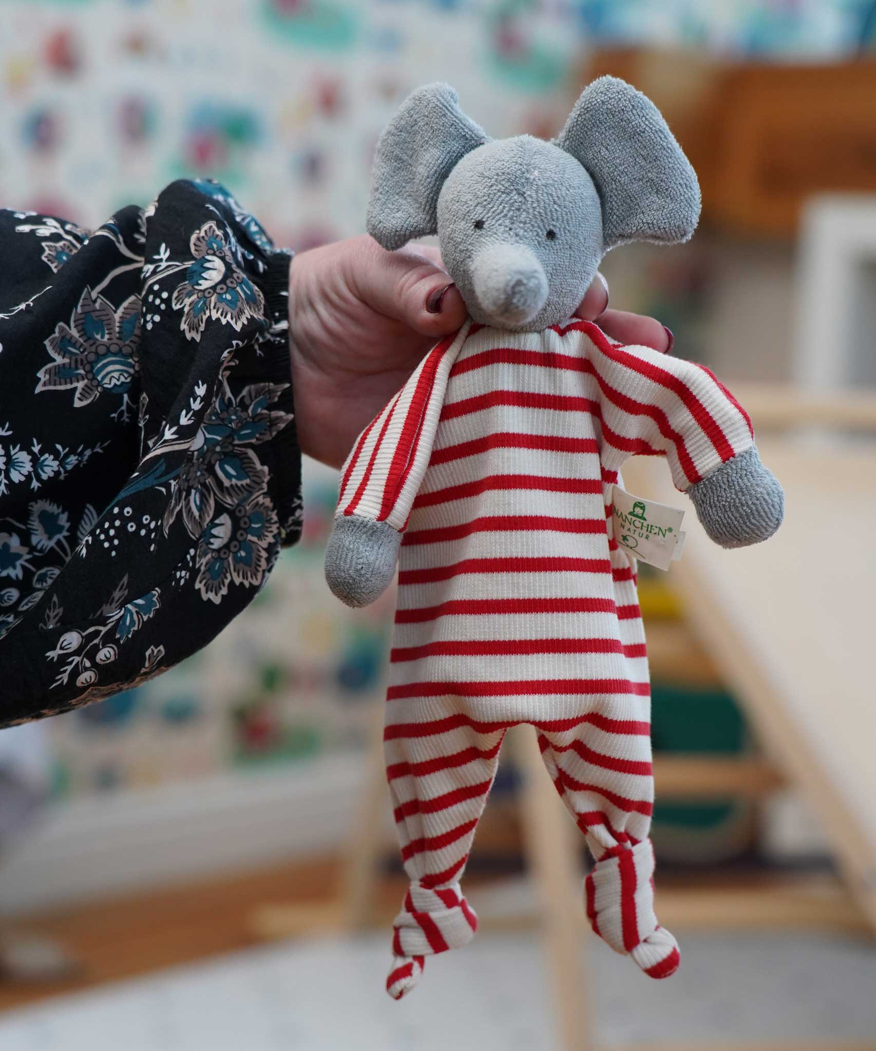 A close up of the Nanchen elephant baby comforter soft toy shown in an adult's hand.