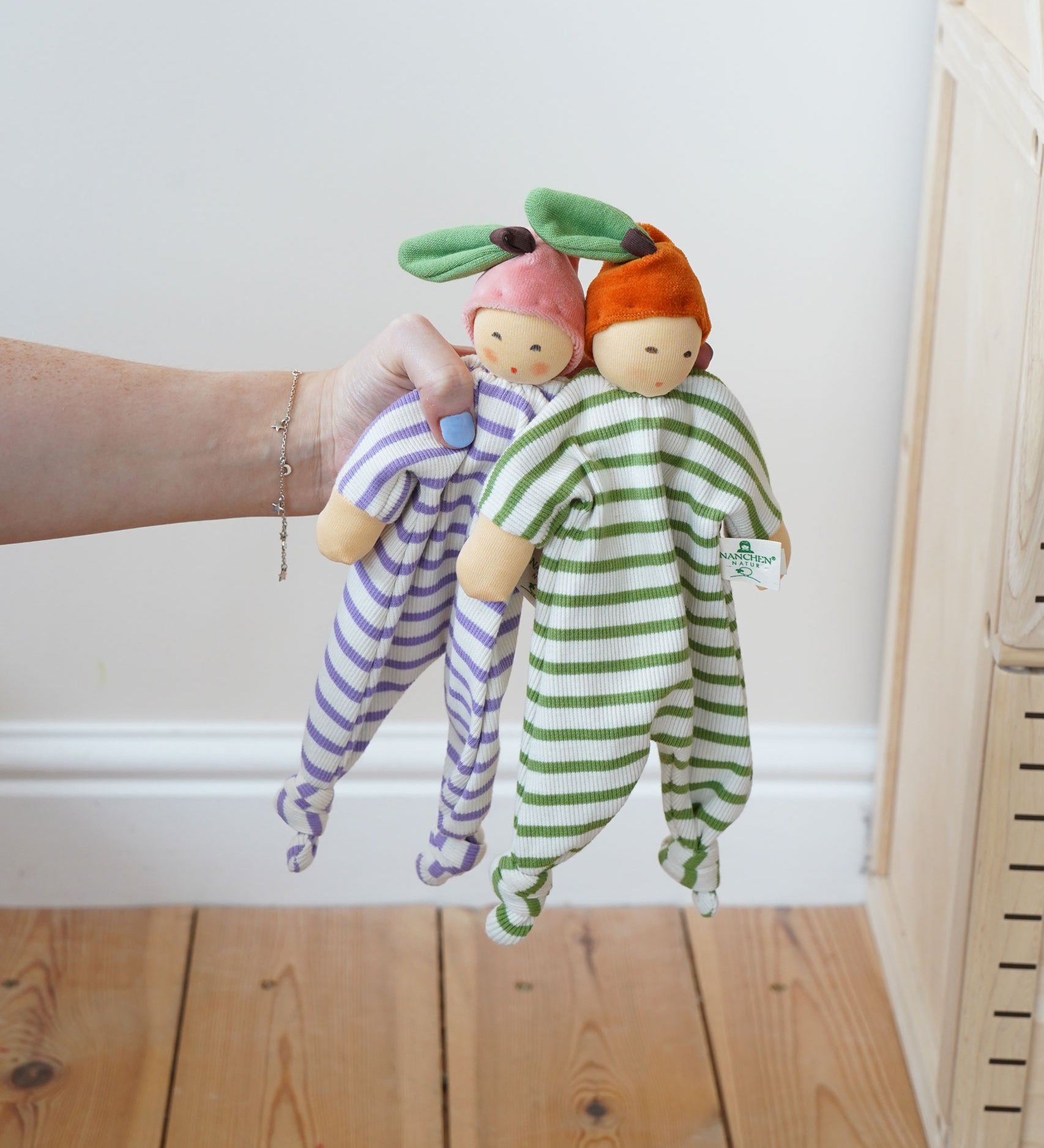 Nanchen peach and orange Baby Comforter Dolls being held up in an adult's hand.