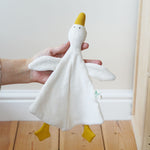 A Nanchen white goose baby comforter being held up in an adult's hand. 