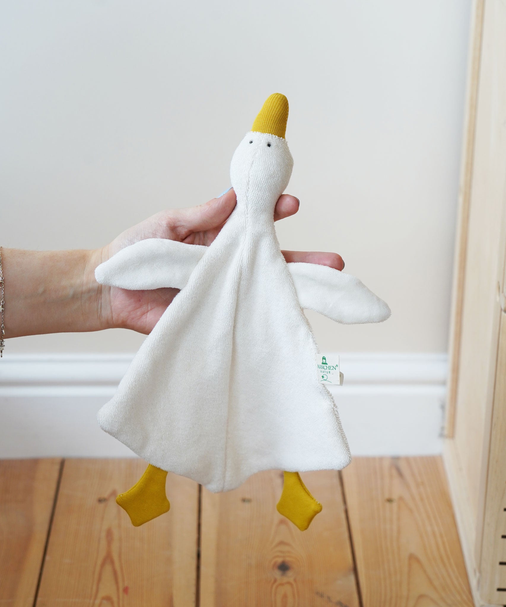 A Nanchen white goose baby comforter being held up in an adult's hand. 