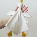 A Nanchen white goose baby comforter being held up in an adult's hand. 