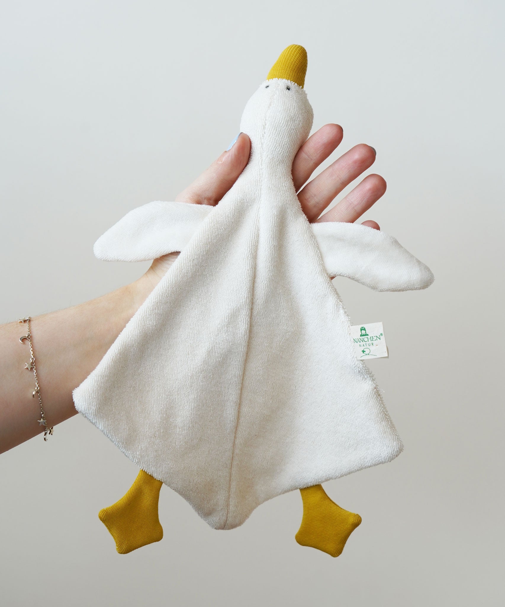 A Nanchen white goose baby comforter being held up in an adult's hand. 