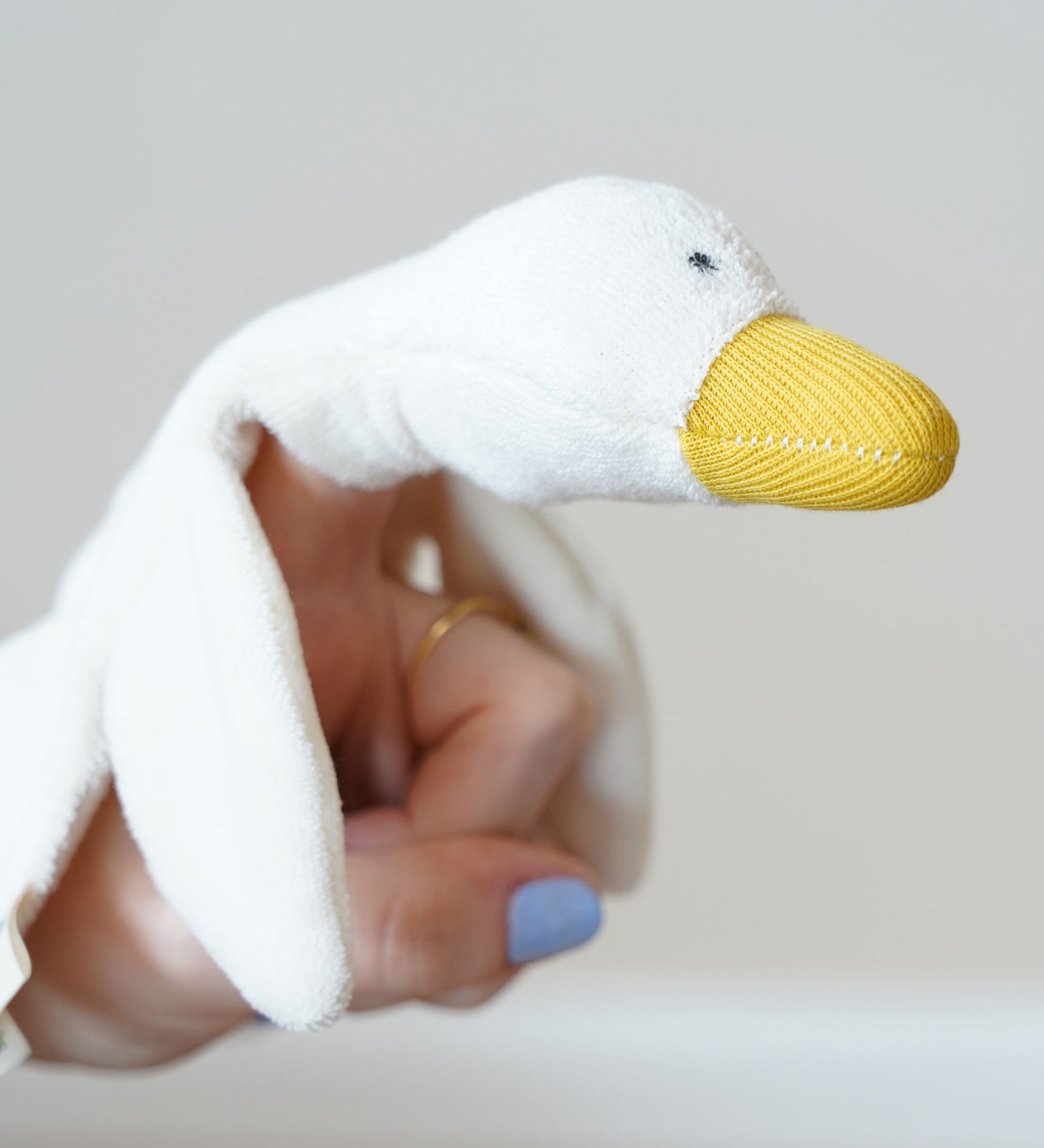 A close up of the goose's head on the Nanchen white goose baby comforter. There is a small pocket in the material allowing the goose to be used as a puppet.