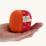 Nanchen Large Colourful, Organic Baby Rattle Ball on a hand for scale. This is a soft terry material in red, orange and pink colours on a cream background.