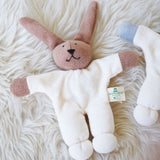 A Nanchen Rabbit Teddy Rattle placed on a sheepskin rug. This rabbit rattle toy is a apart of a range of handcrafted, organic soft toys here at Babipur. 