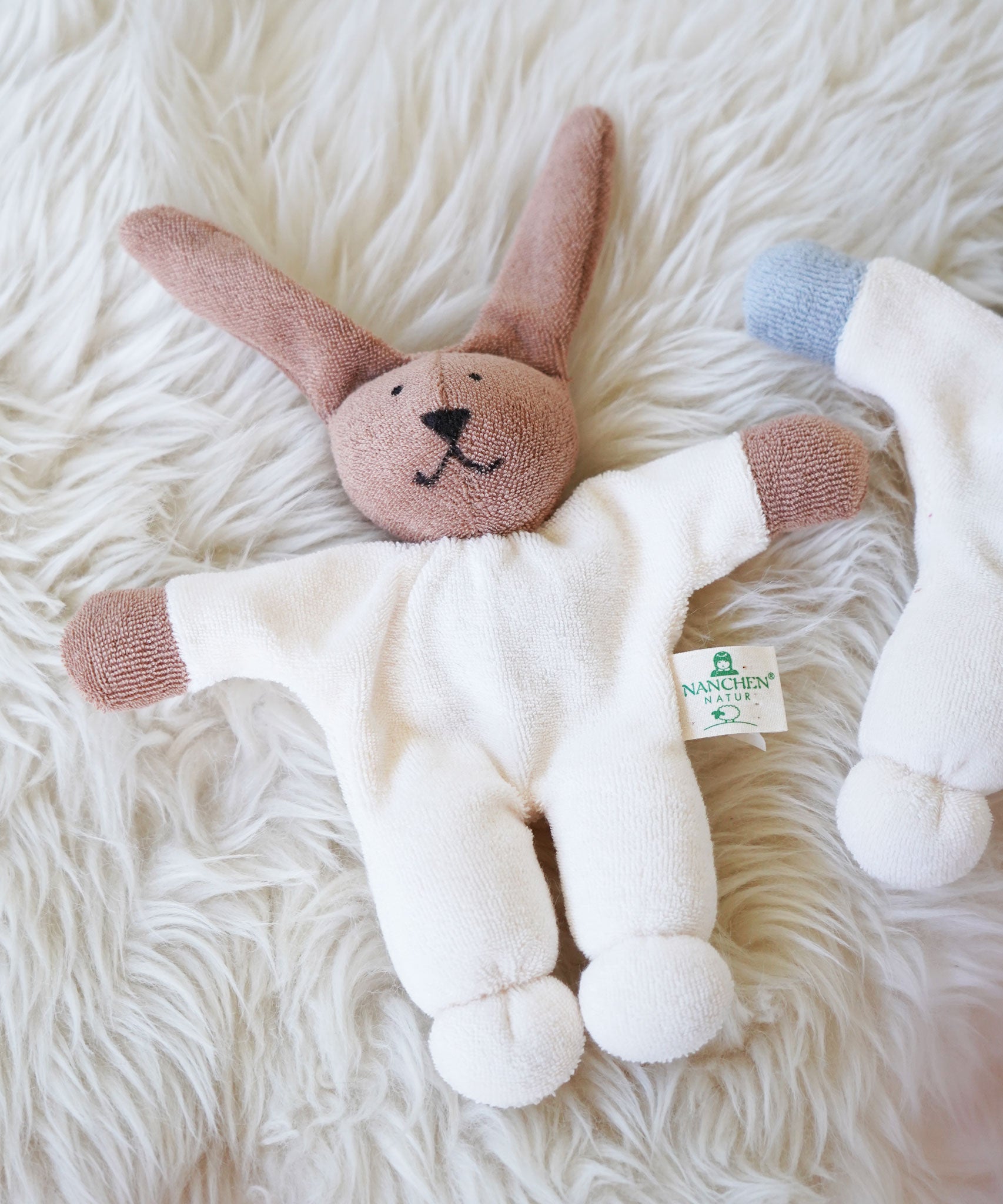 A Nanchen Rabbit Teddy Rattle placed on a sheepskin rug. This rabbit rattle toy is a apart of a range of handcrafted, organic soft toys here at Babipur. 