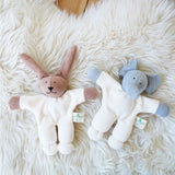 A Nanchen Rabbit and elephant Teddy Rattles placed on a sheepskin rug. These rattle toys are a part of a range of handcrafted, organic soft toys here at Babipur. 
