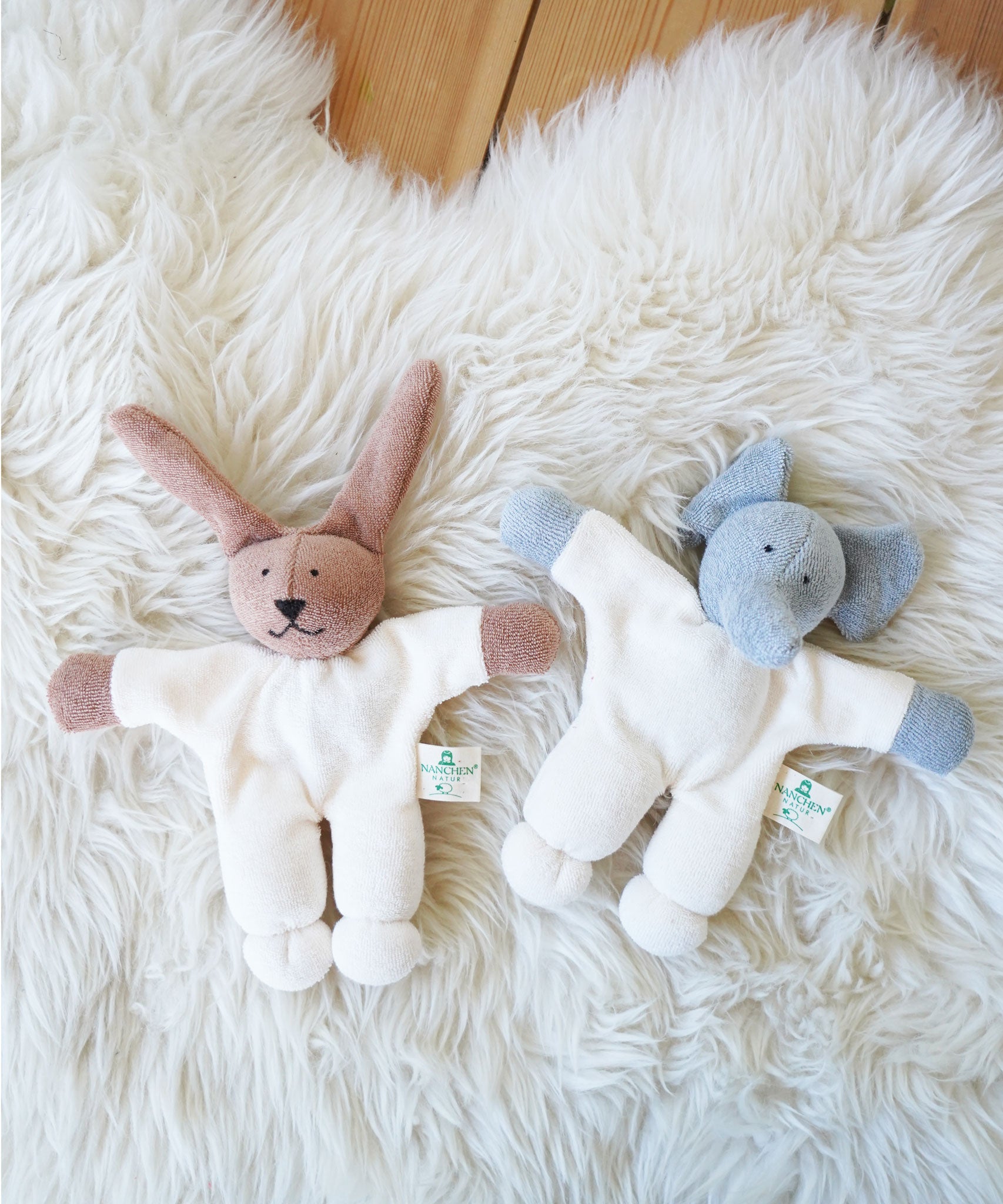 A Nanchen Rabbit and elephant Teddy Rattles placed on a sheepskin rug. These rattle toys are a part of a range of handcrafted, organic soft toys here at Babipur. 