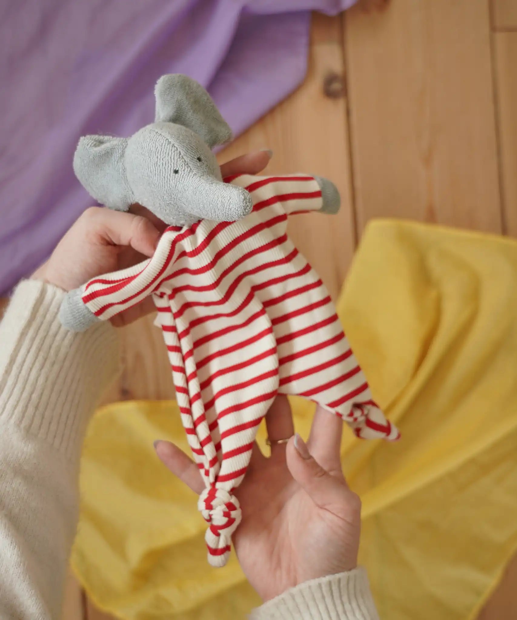 Nanchen elephant striped baby comforter doll in an adult's hand in the Babipur playroom.