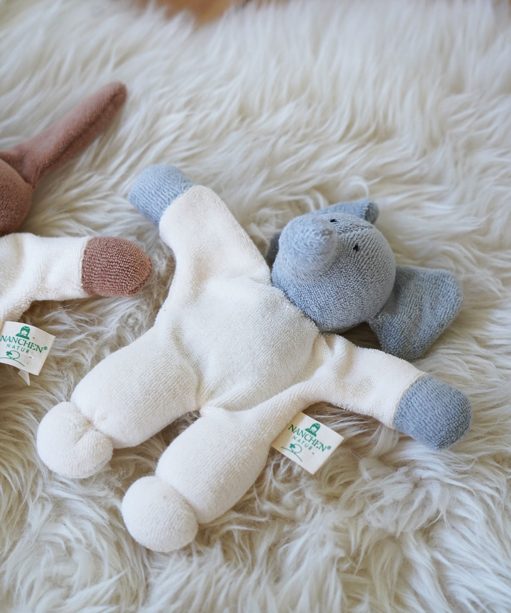 A Nanchen Elephant Teddy Rattle placed on a sheepskin rug.