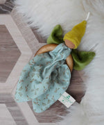 A Nanchen green Flower Fairy Ring Grasper placed on a rug on a wooden floor. A soft toy attached to a wooden ring that can be used as a grasping toy or hung up.