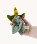 The Nanchen green Flower Fairy Ring Grasper toy shown in an adult's hand. A soft toy attached to a wooden ring that can be used as a grasping toy or hung up.