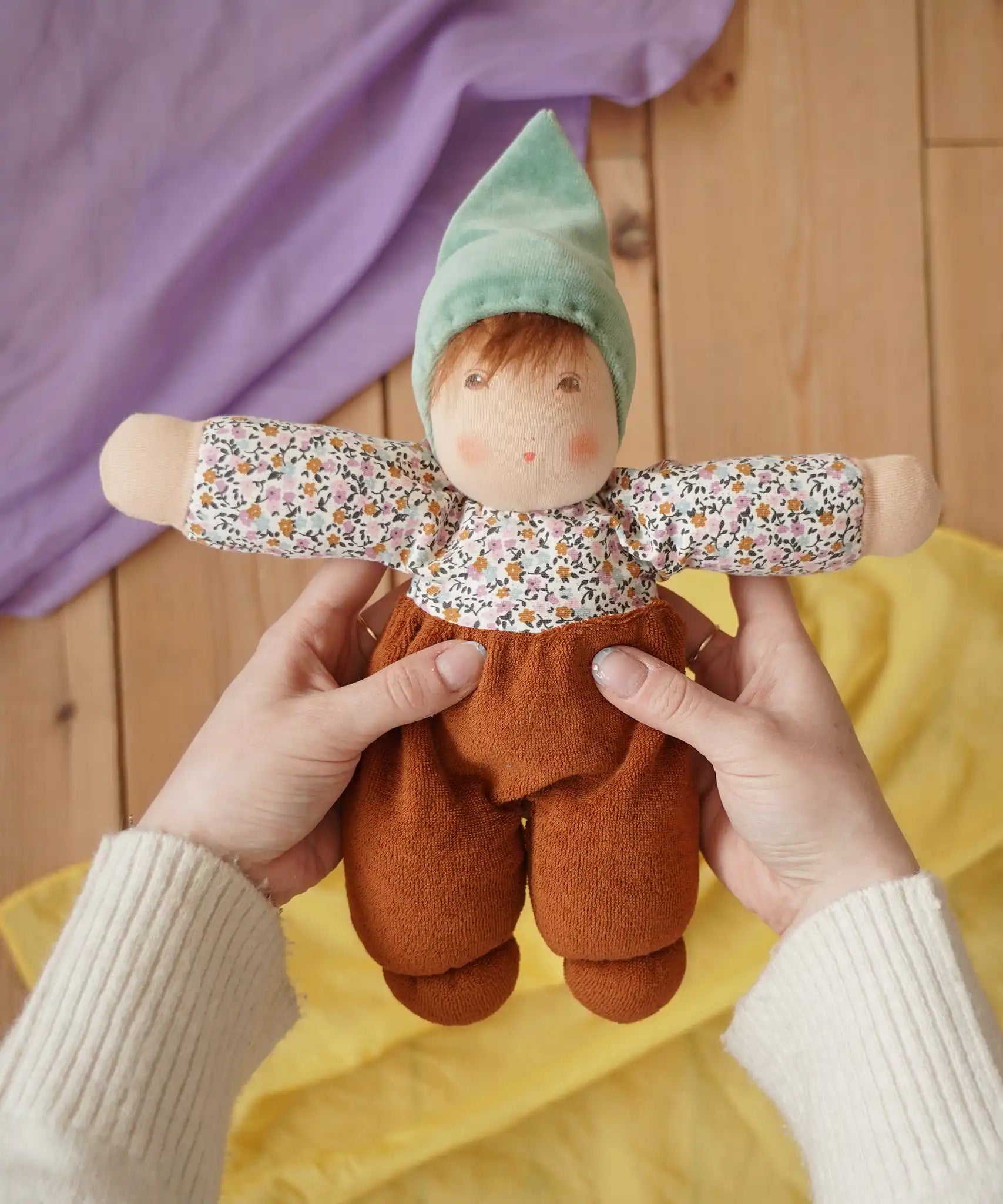 Nanchen Forest Child Waldorf doll in brown in an adult's hand in the Babipur playroom.