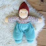A sage Nanchen Forest Child Waldorf Doll placed on a sheepskin rug on a wooden floor.