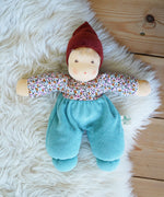 A sage Nanchen Forest Child Waldorf Doll placed on a sheepskin rug on a wooden floor.