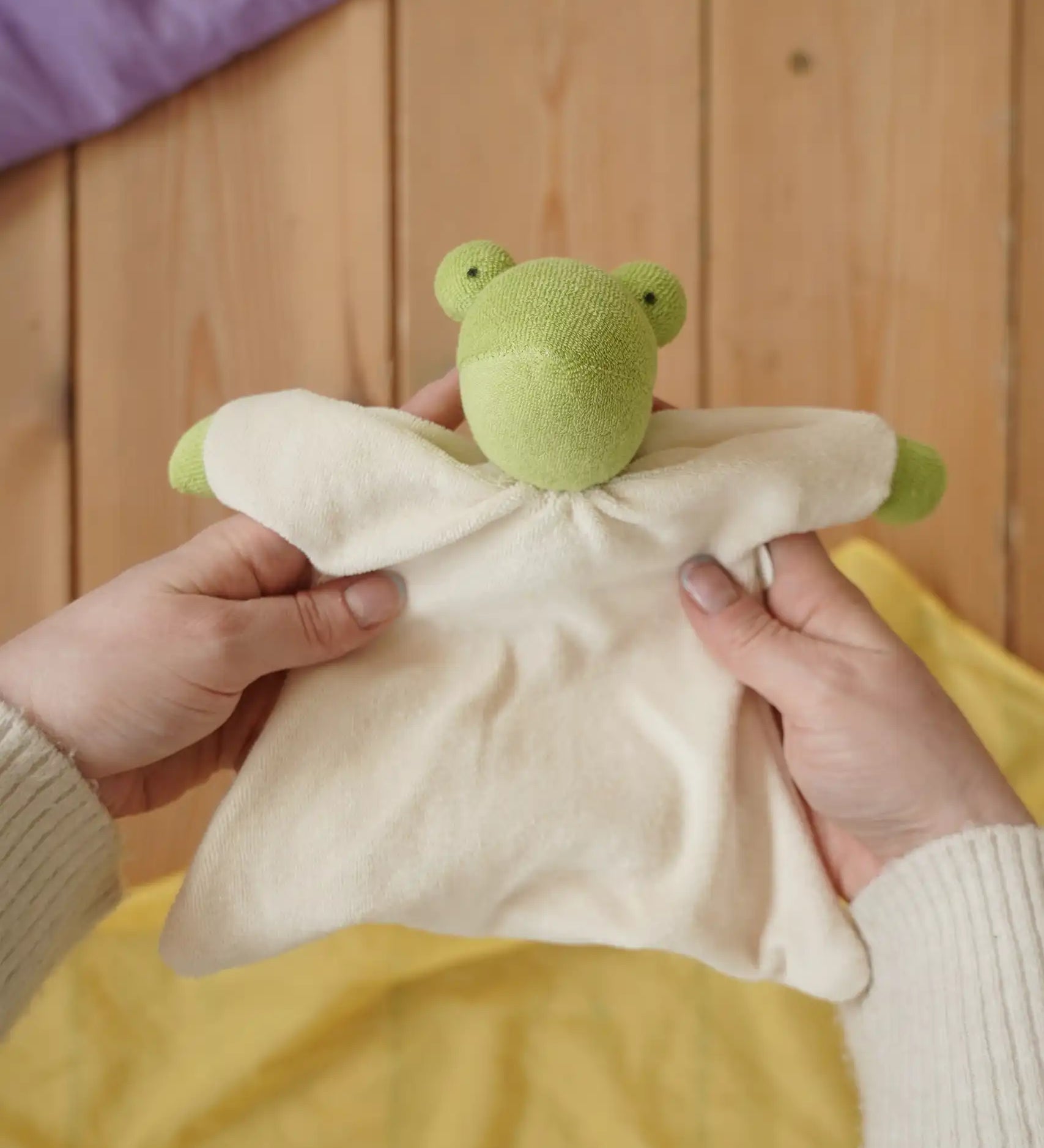 Nanchen Natur frog toweling baby comforter in an adult's hands in the Babipur playroom. 