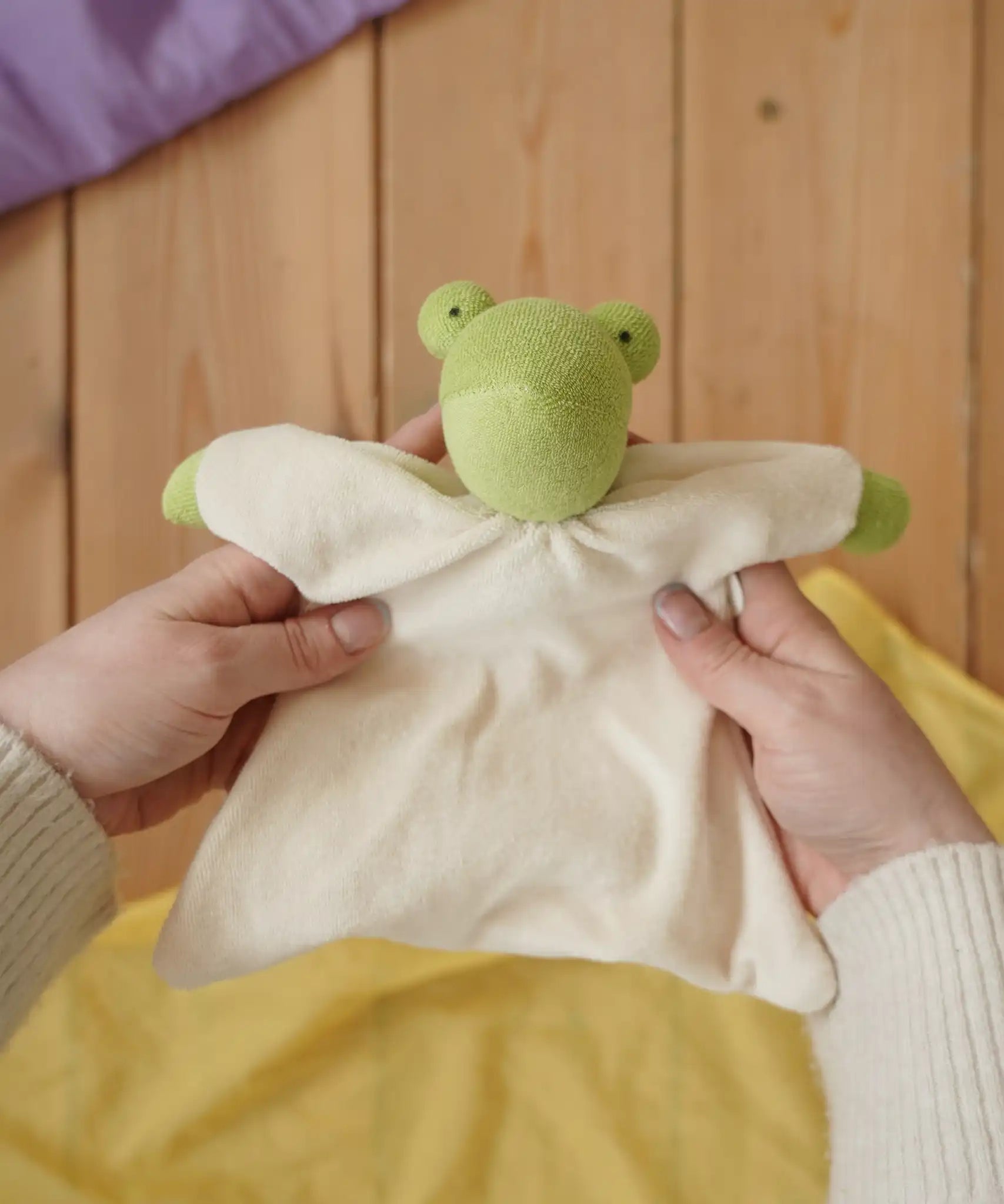 Nanchen Natur frog toweling baby comforter in an adult's hands in the Babipur playroom. 