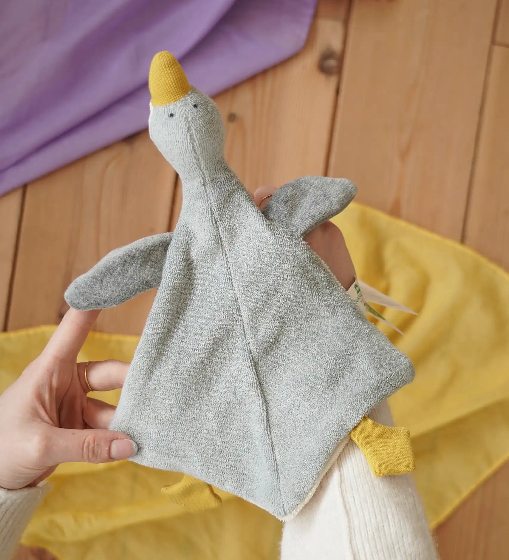 Nanchen grey goose baby comforter shown on an adult's hand in the Babipur playroom. 