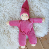 A pink Nanchen Nani Waldorf Doll placed on a sheepskin rug on a wooden floor.