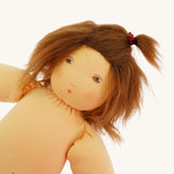 A close up of the head of the  Nanchen handcrafted Little Red Riding Hood Waldorf doll. The doll has brown eyes an hair and is wearing a small red bobble in her hair.