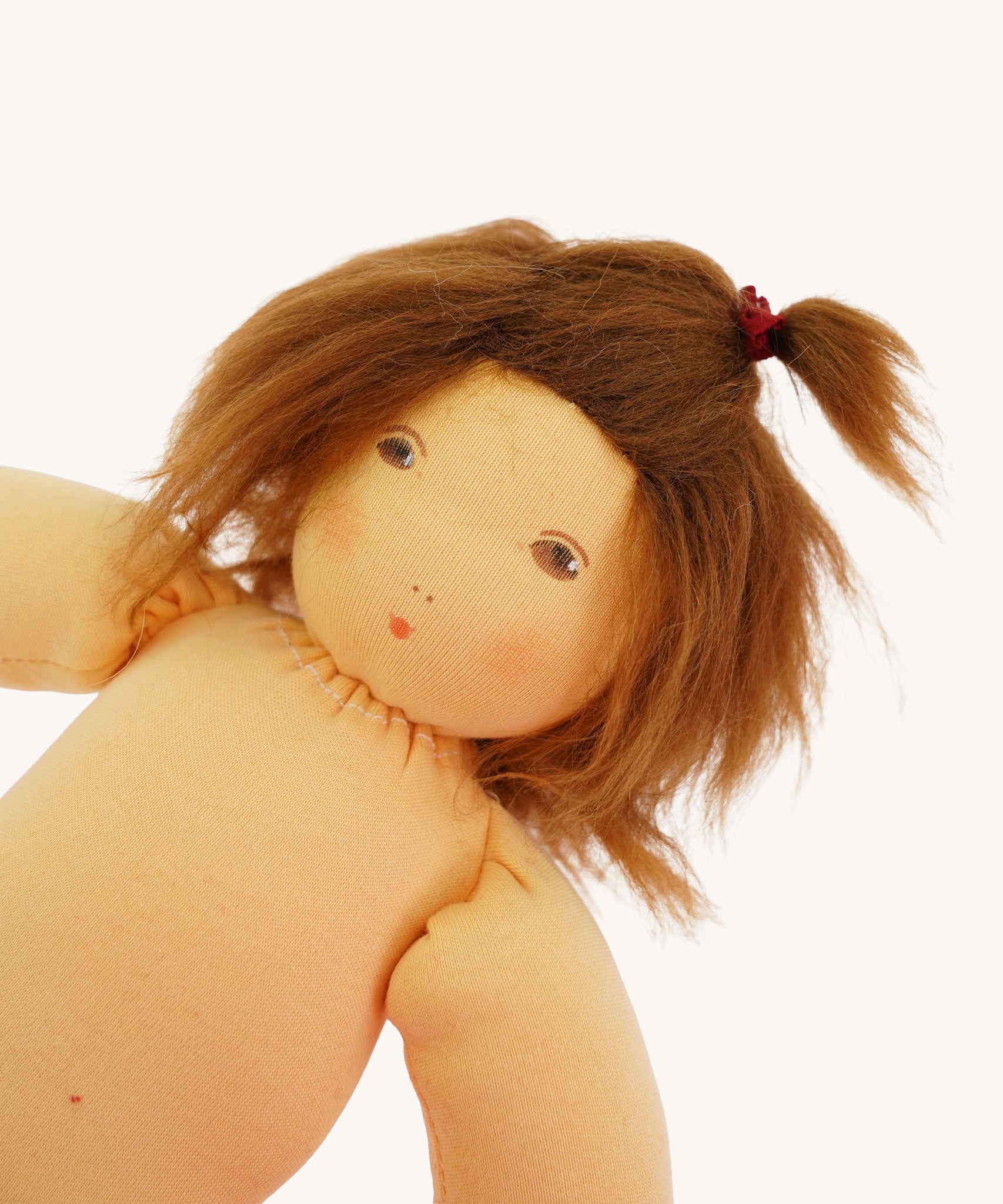 A close up of the head of the  Nanchen handcrafted Little Red Riding Hood Waldorf doll. The doll has brown eyes an hair and is wearing a small red bobble in her hair.