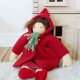A Nanchen handcrafted Little Red Riding Hood Waldorf doll placed in a seated position leaning against a PlanToys Victorian dolls house.