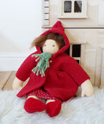 A Nanchen handcrafted Little Red Riding Hood Waldorf doll placed in a seated position leaning against a PlanToys Victorian dolls house.