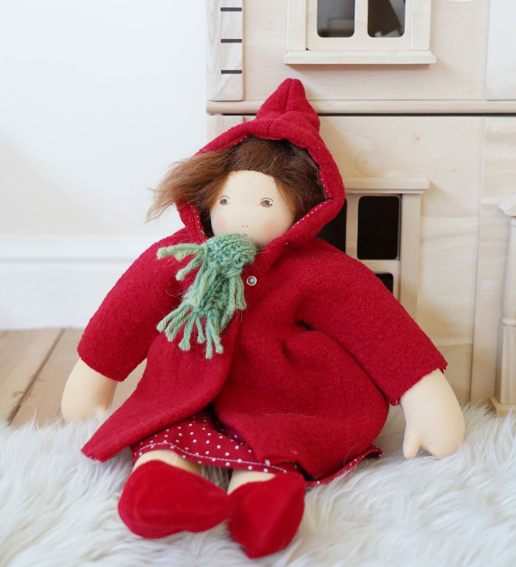 A Nanchen handcrafted Little Red Riding Hood Waldorf doll placed in a seated position leaning against a PlanToys Victorian dolls house.