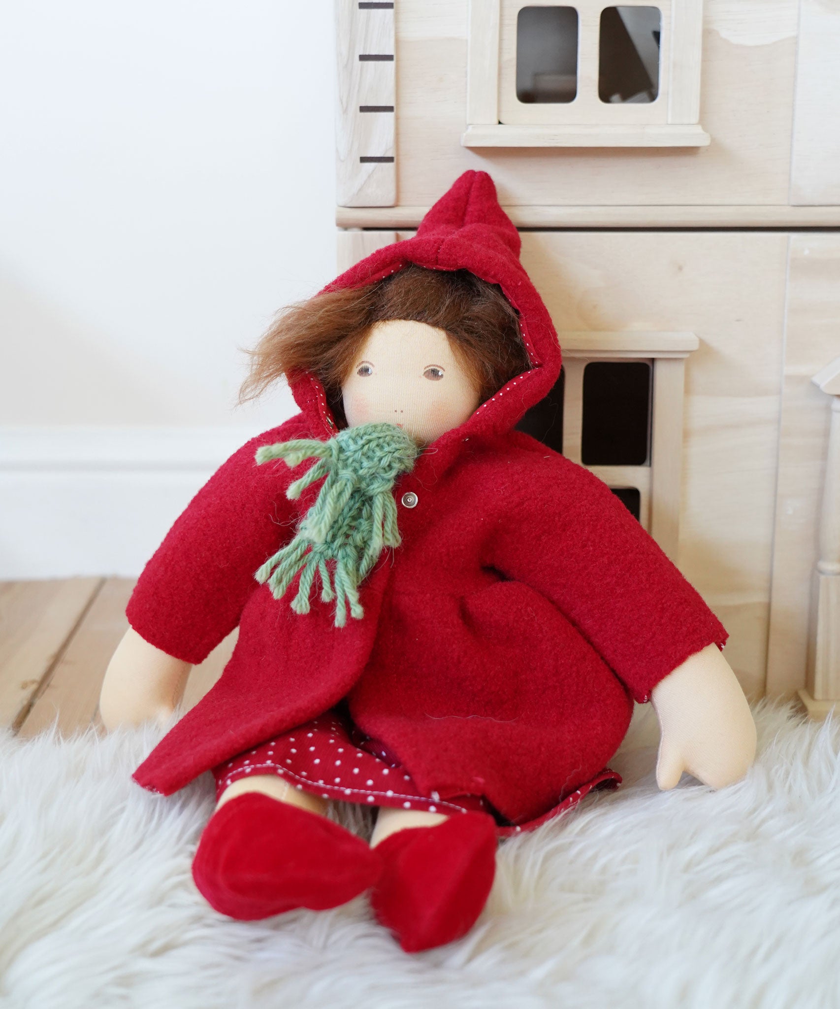 A Nanchen handcrafted Little Red Riding Hood Waldorf doll placed in a seated position leaning against a PlanToys Victorian dolls house.