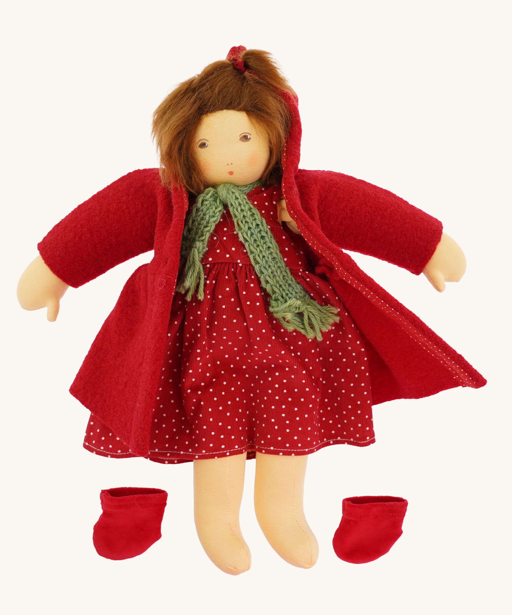 The Nanchen handcrafted Little Red Riding Hood Waldorf doll shown with the red coat opened revealing the spotty cord dress underneath. The doll's shoes have been removed and placed besides her.