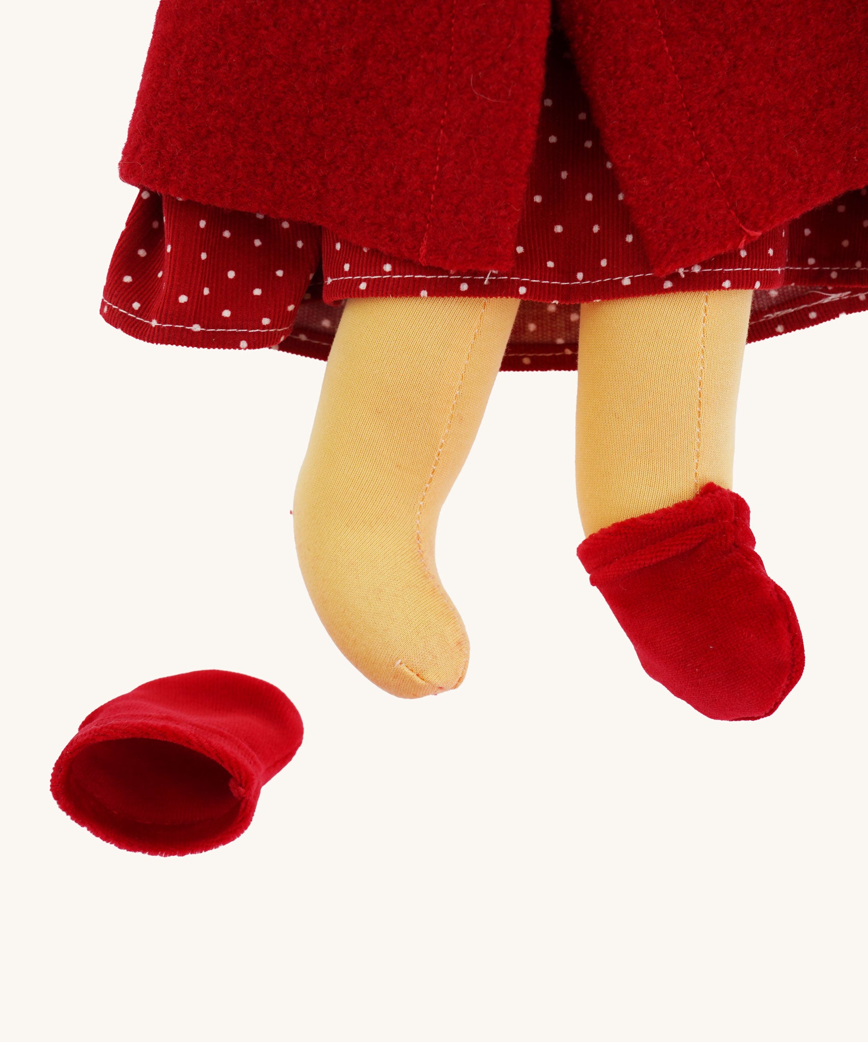 A close up of the  Nanchen handcrafted Little Red Riding Hood Waldorf doll's feet. The doll has one red coloured velvet slipper type shoe on and one off. 