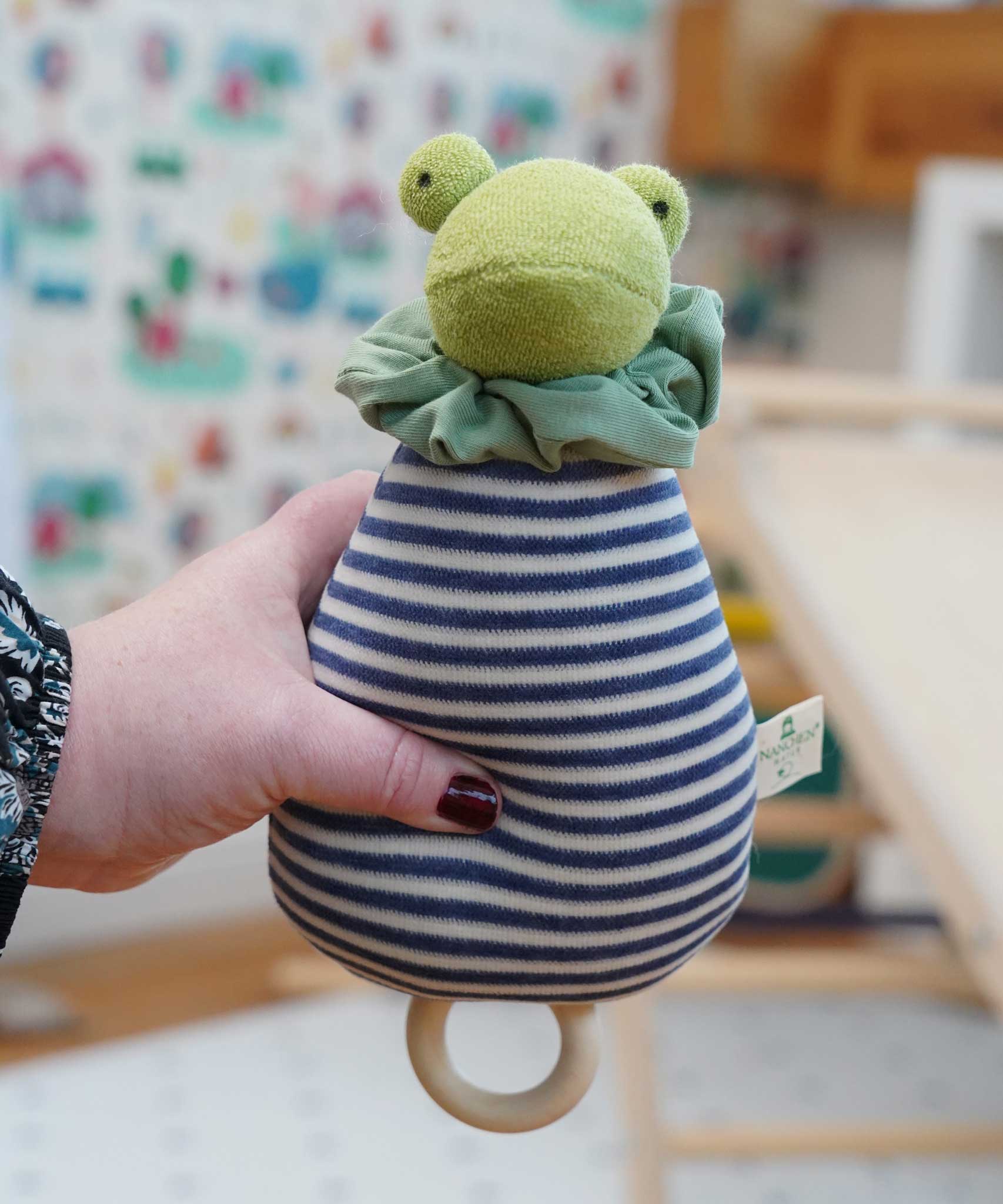 The Nanchen Brave Little Frog Lullaby Music Doll shown in an adult's hand. A musical Waldorf doll, made from organic cotton and sheep's wool. 
