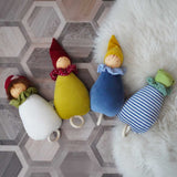 A collection of four Nanchen Lullaby Music Dolls. Musical Waldorf dollS, made from organic cotton and sheep's wool. The toadstool, little red riding hood, blue dream kings and frog lullaby dolls have been placed on a rug on a wooden floor. 