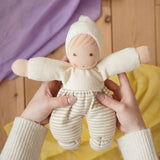 Nanchen Möpschen Waldorf doll in natural white colour with striped pattern on trousers in an adult's hand in the Babipur playroom.

