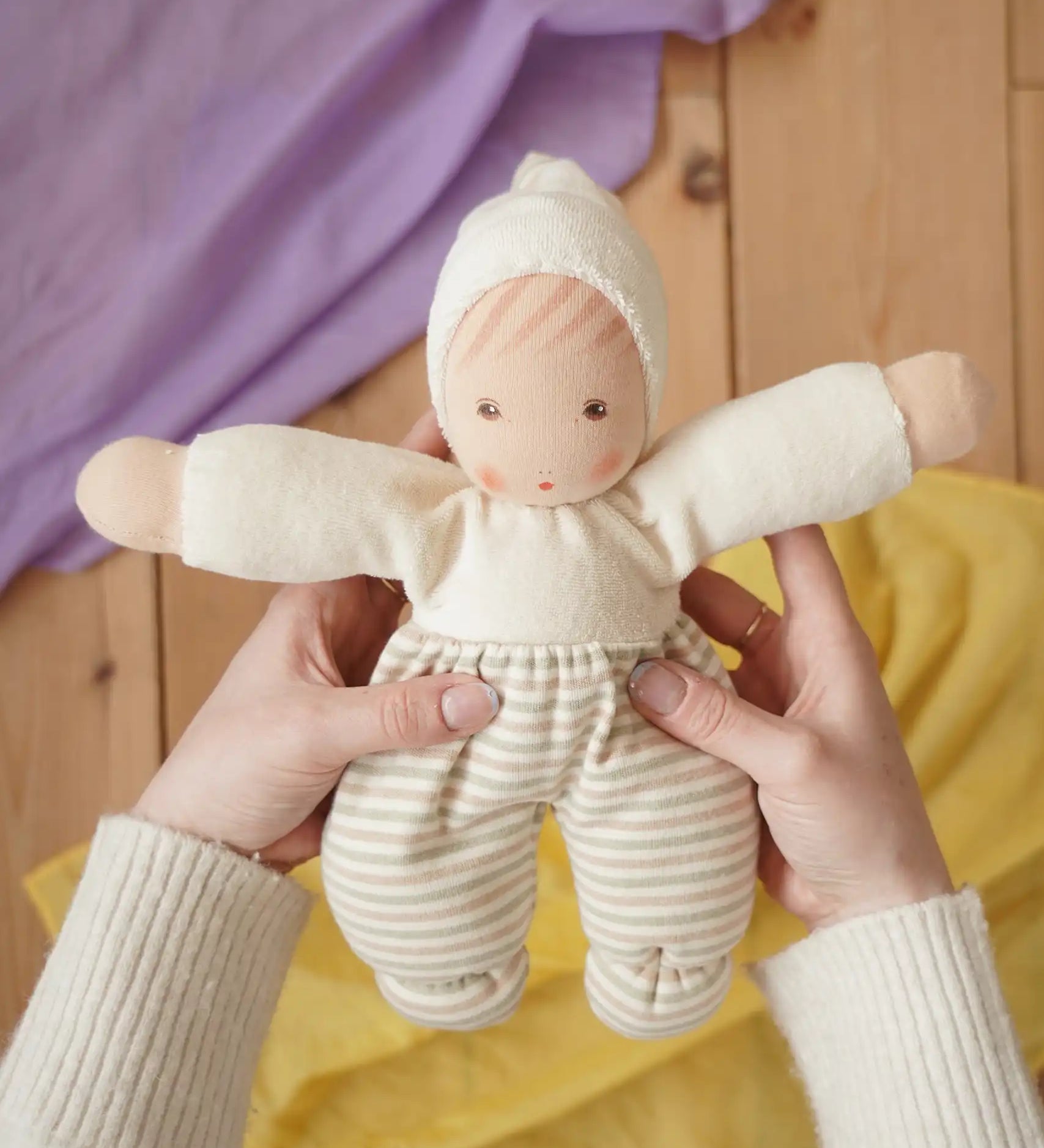 Nanchen Möpschen Waldorf doll in natural white colour with striped pattern on trousers in an adult's hand in the Babipur playroom.
