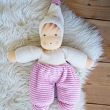 A Nanchen Möpschen Waldorf Doll with Pink Stripes placed on a sheepskin rug on a wooden floor.