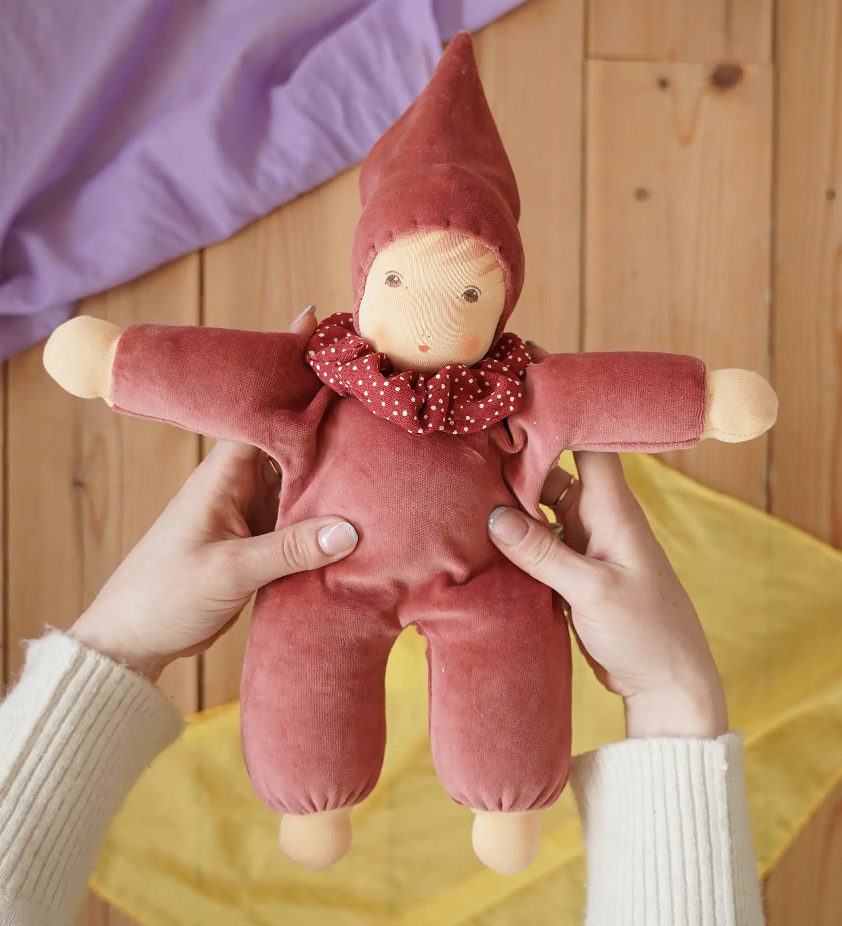 Nanchen Natur Nani Waldorf doll in cedar pink in an adult's hands in the Babipur playroom. 