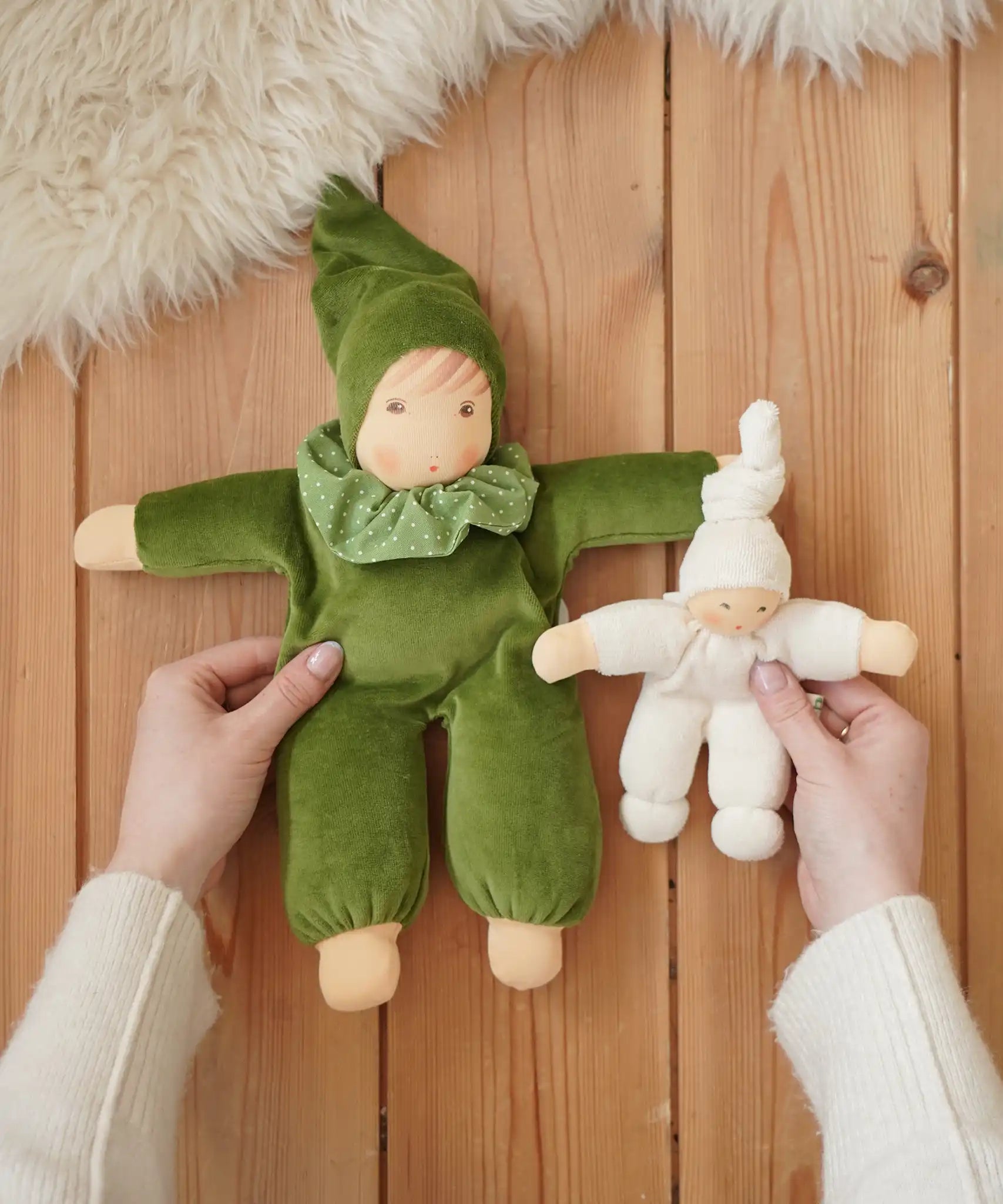 Nanchen Natur Waldorf Nani doll in forest green and a natural pimpel dolls in an adult's hands in the Babipur playroom. 