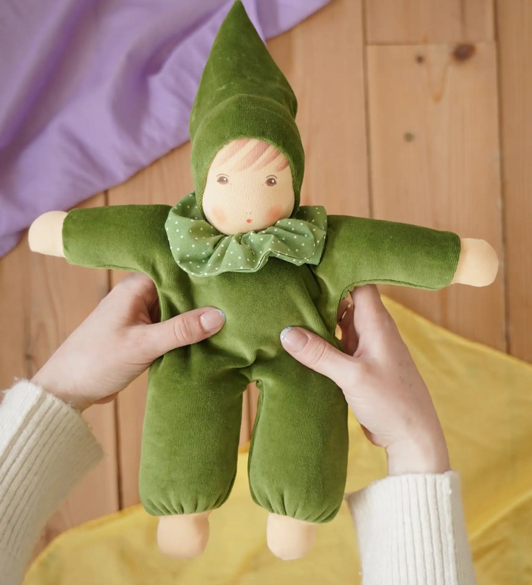 Nanchen Natur Waldorf Nani doll in forest green in an adult's hands in the Babipur playroom. 