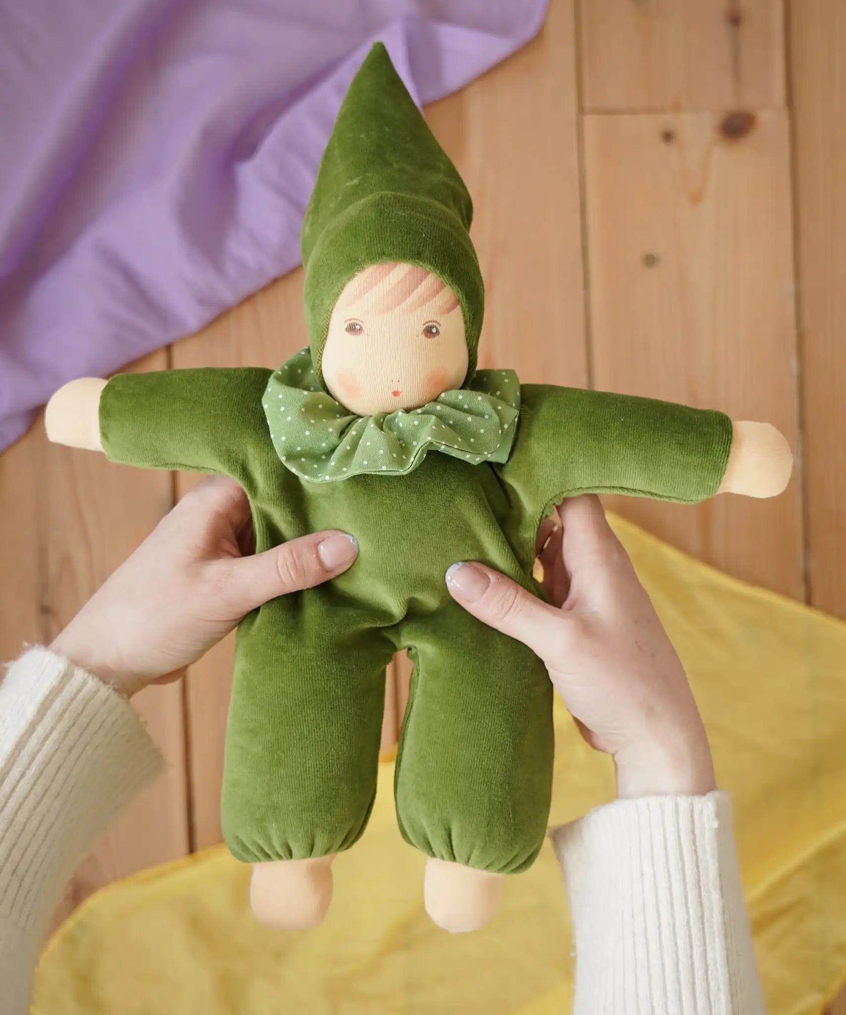 Nanchen Natur Waldorf Nani doll in forest green in an adult's hands in the Babipur playroom. 