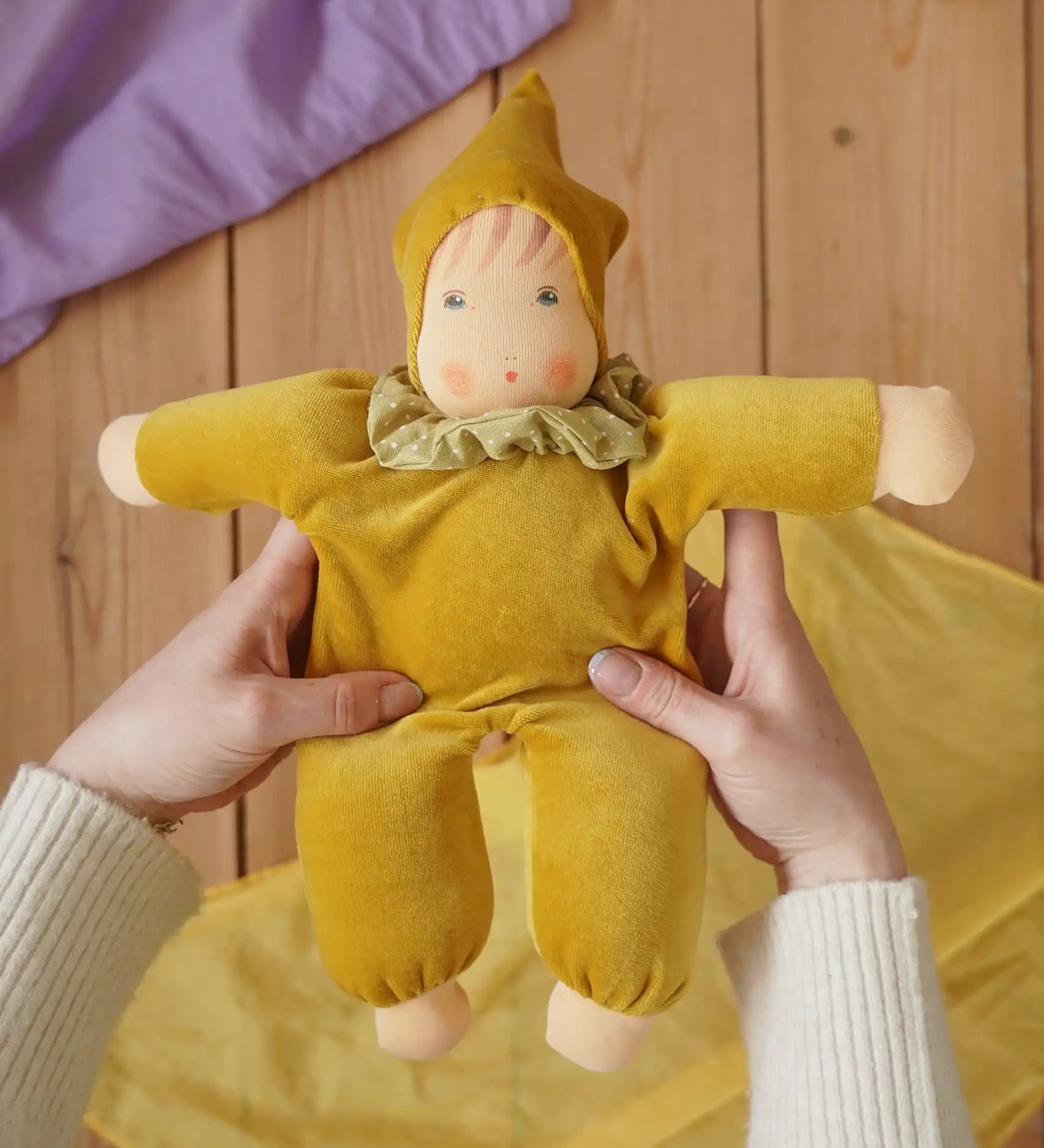 Nanchen Natur Nani Waldorf doll in gold in an adult's hand in the Babipur playroom. 