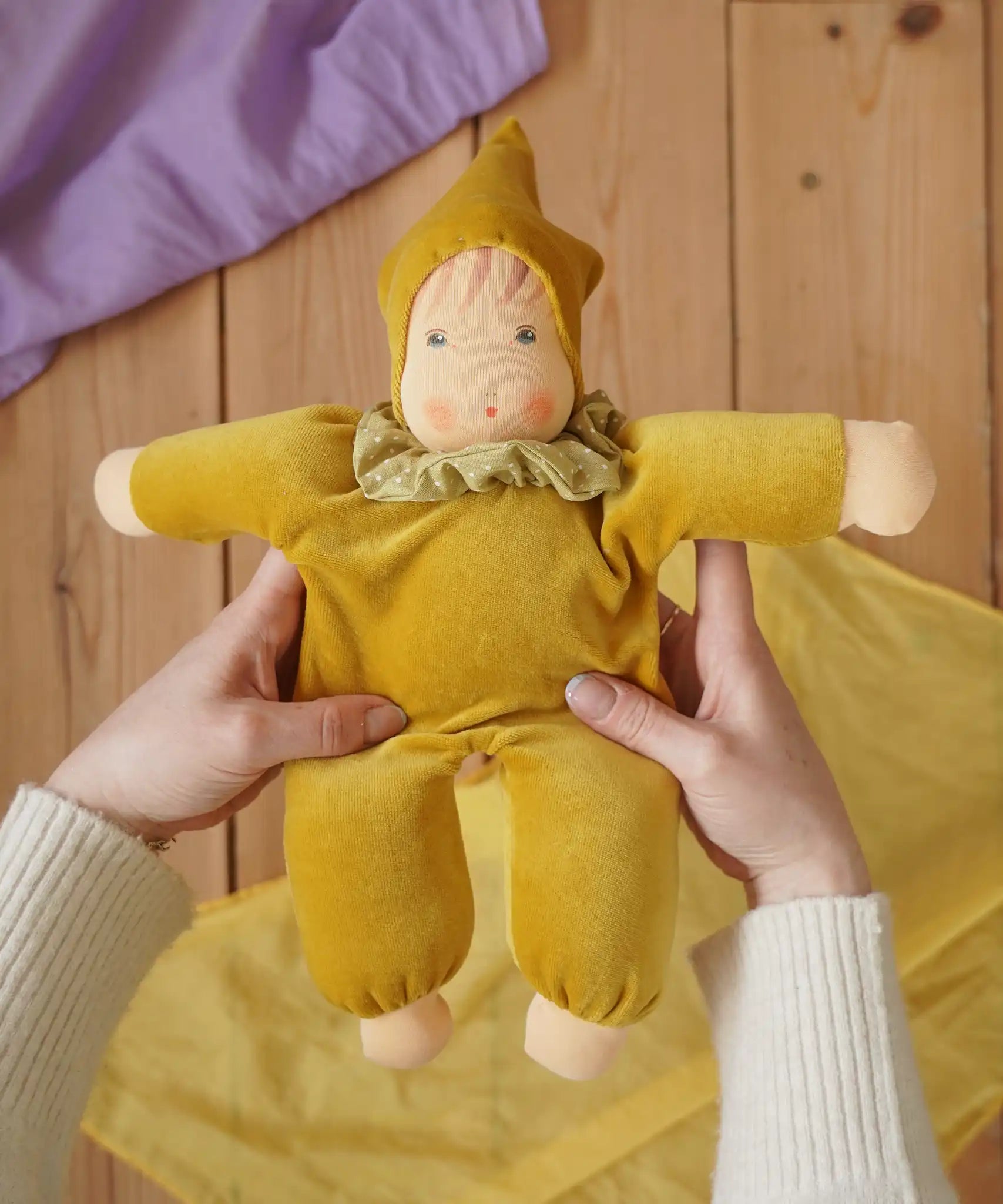 Nanchen Natur Nani Waldorf doll in gold in an adult's hand in the Babipur playroom. 