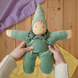 Nanchen Natur Waldorf Nani doll in mint green in an adult's hands in the Babipur playroom. Purple and yellow Laura's play cloths can be seen in the background.