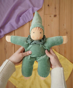 Nanchen Natur Waldorf Nani doll in mint green in an adult's hands in the Babipur playroom. Purple and yellow Laura's play cloths can be seen in the background.