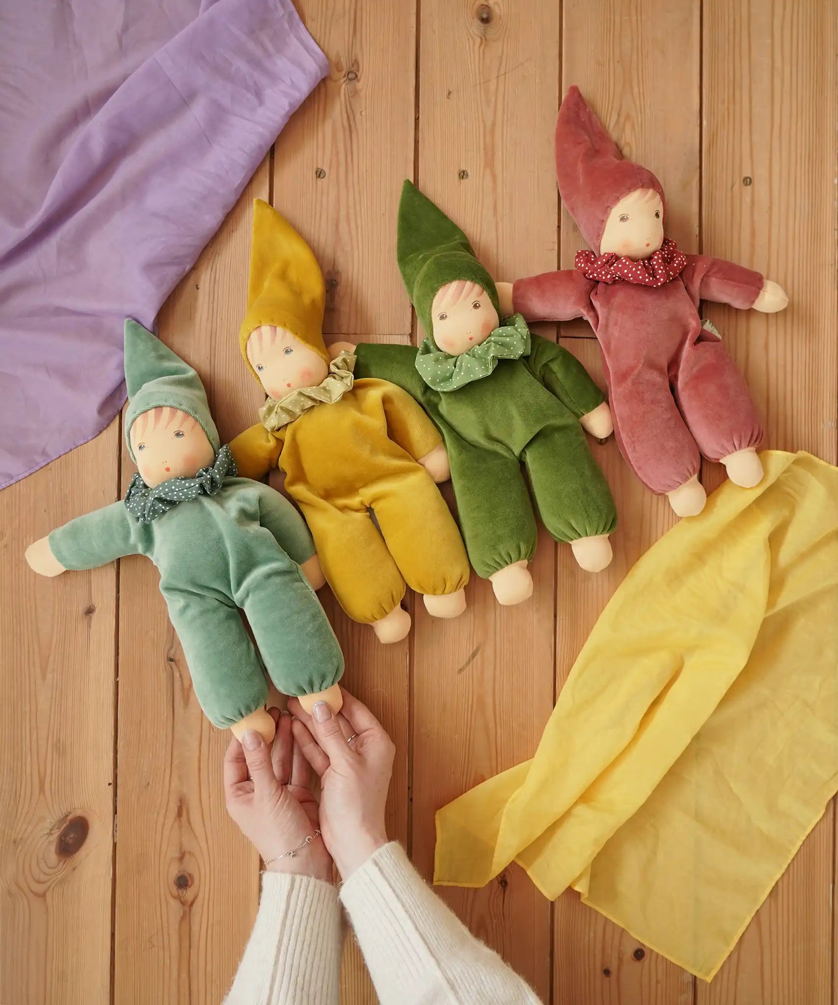 Four Nanchen Natur handmade Nani Waldorf dolls in mint, goldm forest green and cedar pink placed on a wooden floor in the Babipur playroom. 