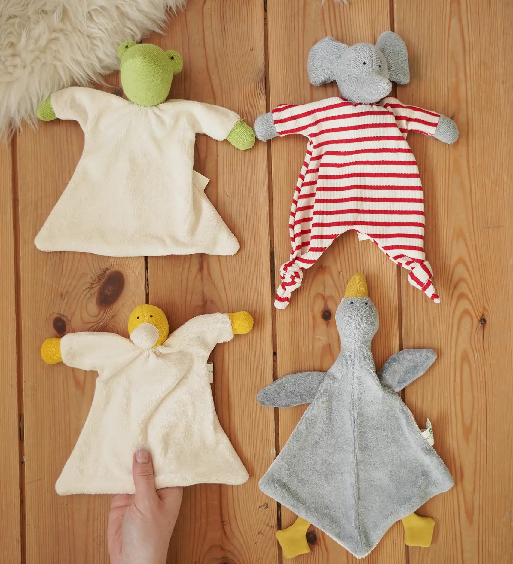 Four Nanchen Natur baby comforters , frog, elephant, duck and goose placed on a wooden floor in the Babipur playroom. 