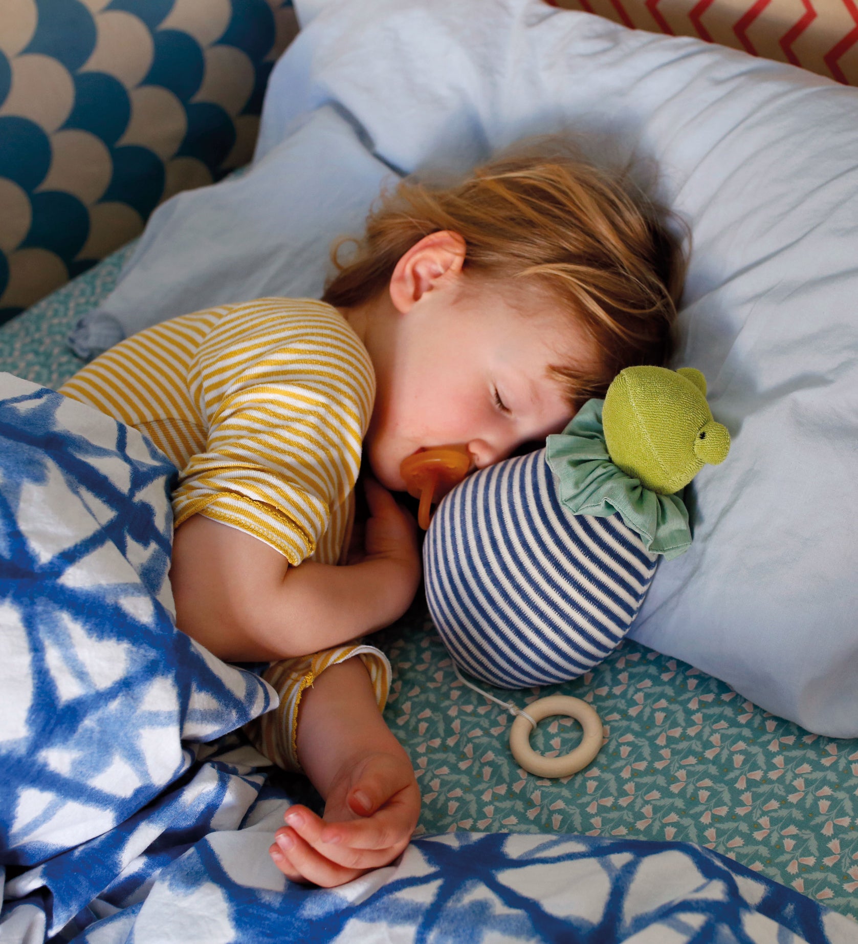 A child having a nap next to his Nanchen Natur 'Brave Little Frog' musical Waldorf doll, made from organic cotton and sheep's wool. 