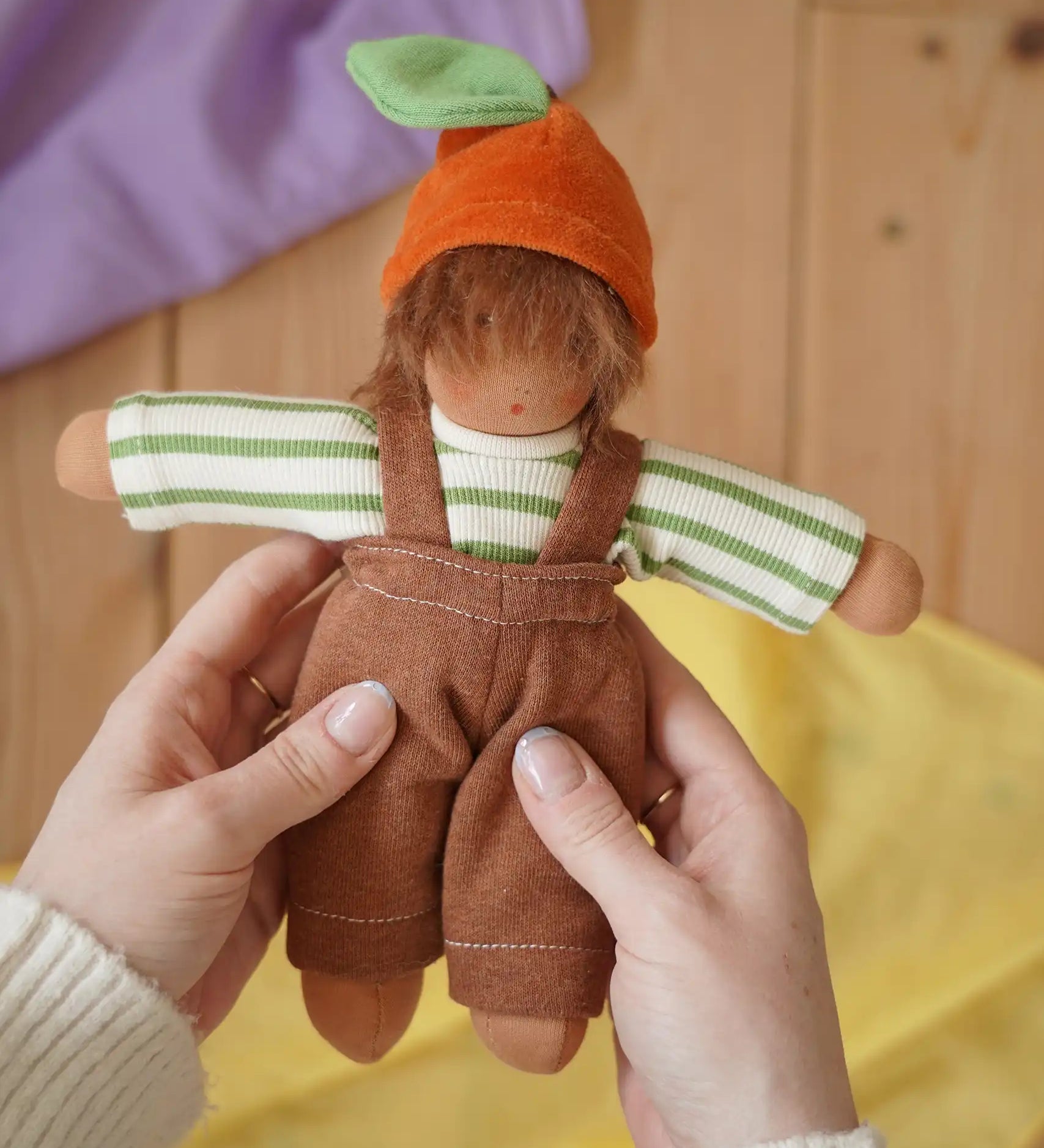 Nanchen Otto Orange child Waldorf doll in an adult's hand in the Babipur playroom.