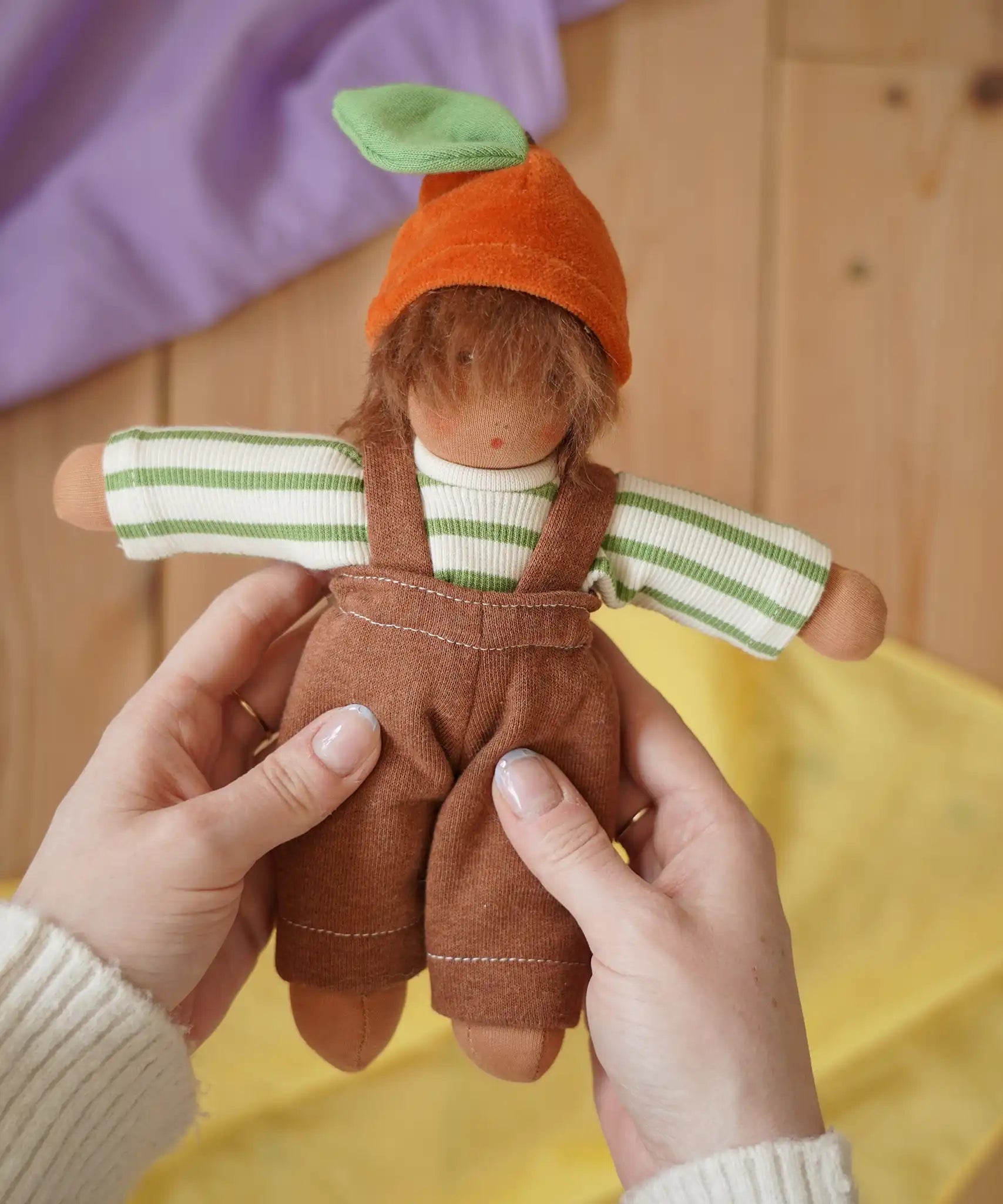 Nanchen Otto Orange child Waldorf doll in an adult's hand in the Babipur playroom.